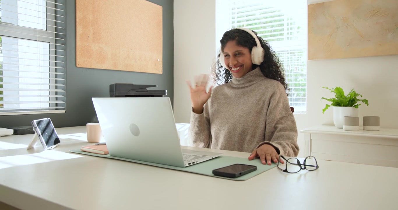 Mujer con cuello alto levantando auriculares, acomodándose en el escritorio y hablando por el portátil discutiendo el trabajo