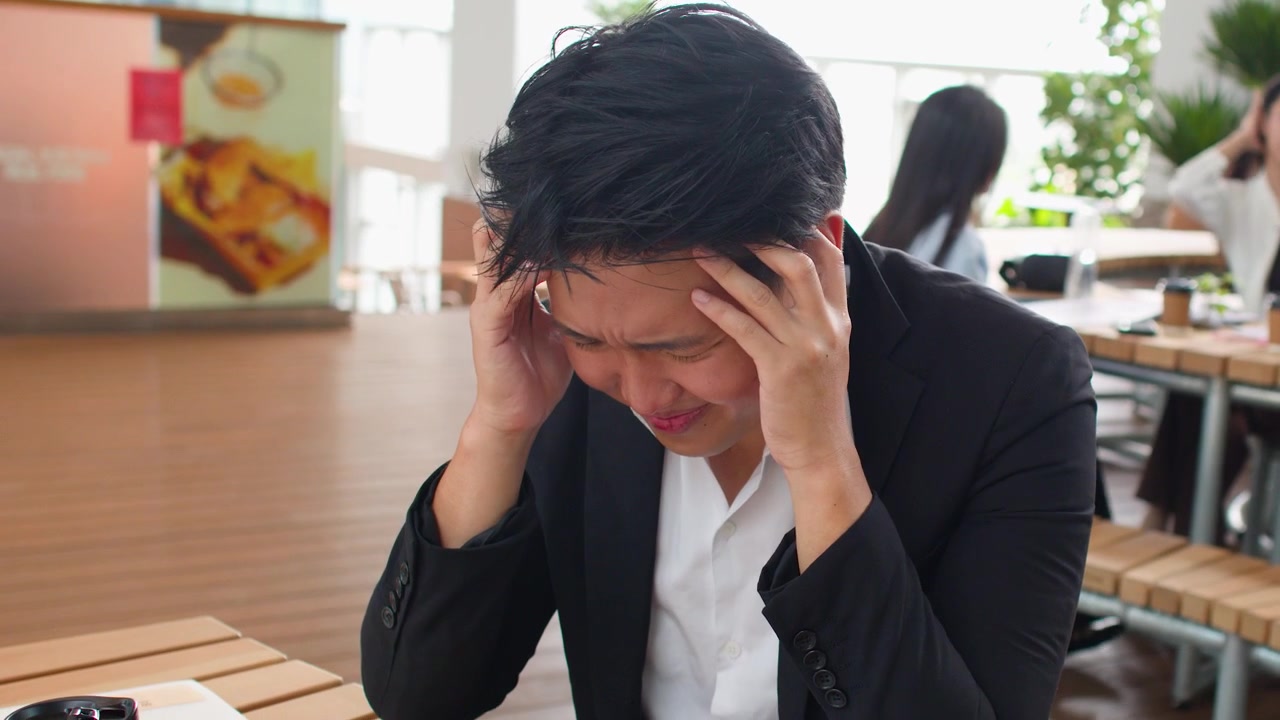 屋外で座っている、黒いスーツ姿の過労のビジネスマンが激しい片頭痛に苦しんでいる。
