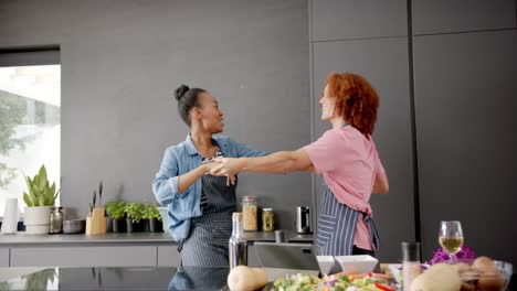 happy diverse couple in aprons having fun cooking and dancing together in kitchen, in slow motion