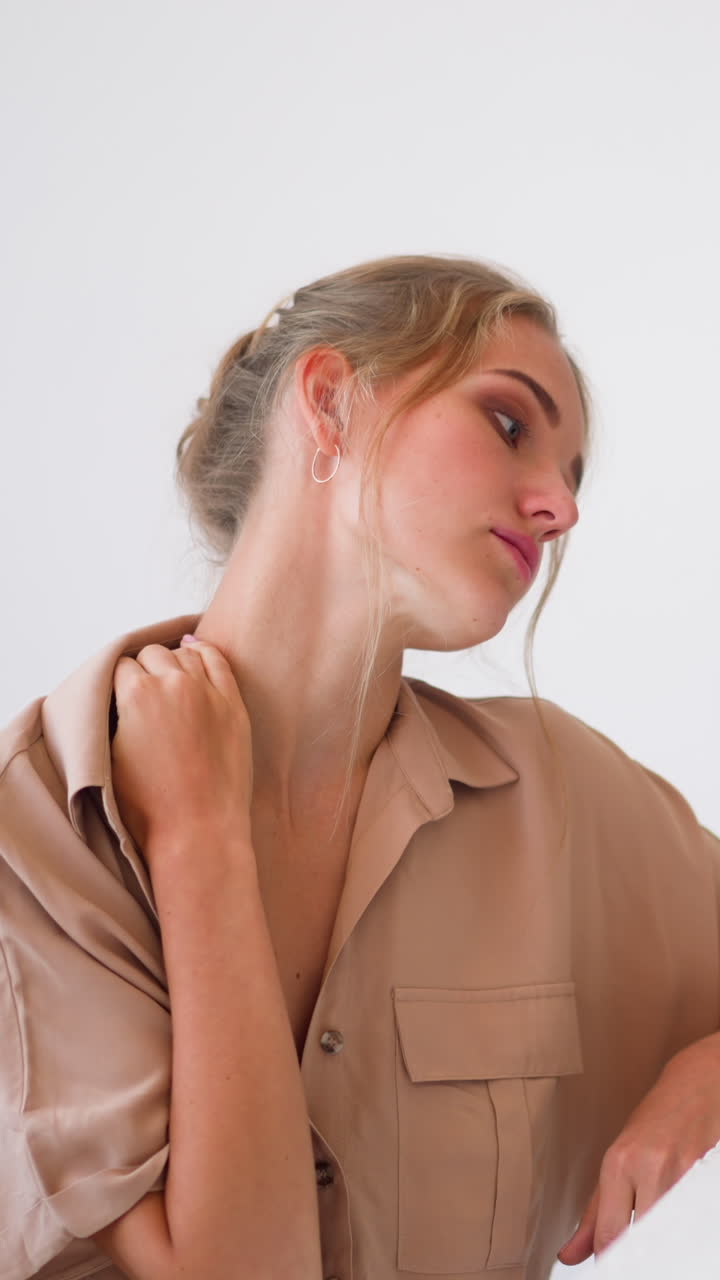Young blonde woman feels tired and massages sore neck with hand working on small laptop at white table in modern home office slow motion