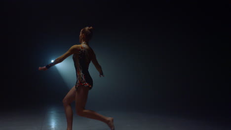 graceful woman jumping in spotlight background. young gymnast dancing indoors.