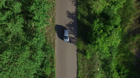 Drone-Ver-Coche-Moviéndose-Por-La-Carretera-Pasando-El-Bosque-De-Verano-En-El-Campo