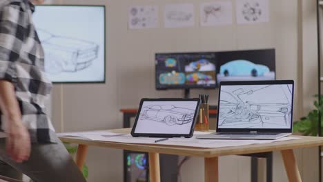vista lateral de un hombre asiático caminando para sentarse y dibujar un nuevo concepto de diseño de automóvil en una tableta en el estudio con televisión y computadoras muestra modelo de automóvil eléctrico 3d