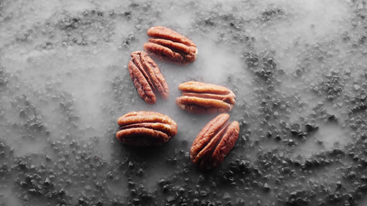 5 nueces de pecan crujientes están siendo asadas en un lecho de rocas negras calientes, nubes de vapor fluyen a su alrededor