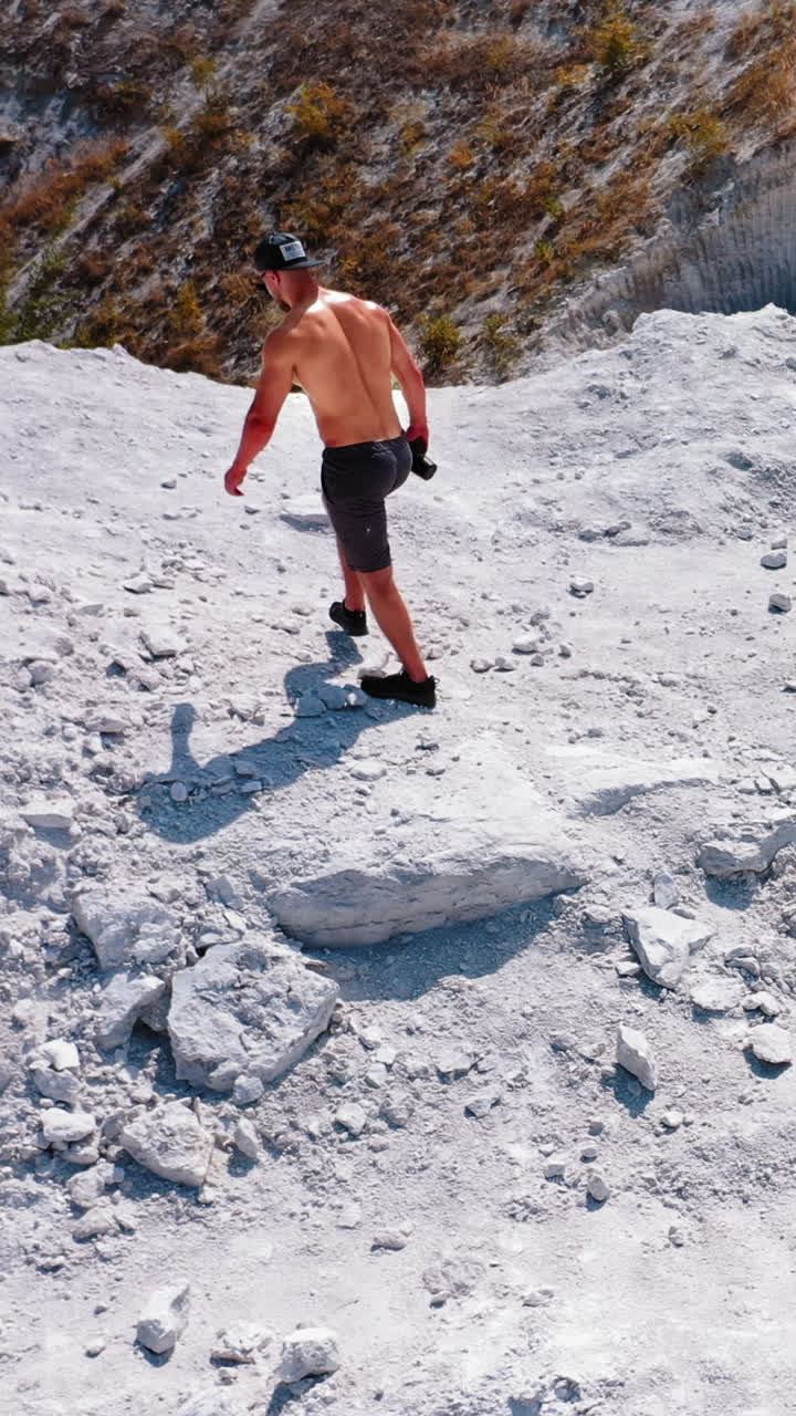 Brutal strong bodybuilder posing outdoor. Photoshoot in a quarry. Outdoor sports concept. Aerial view. Handsome strongman walks up a quarry. White landscape. Vertical video