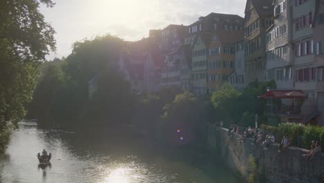 Barco-Que-Pasa-Junto-A-La-Gente-Que-Se-Relaja-En-La-Pared-En-Tubingen,-Alemania-En-4k-En-El-Centro-De-La-Ciudad-De-La-Universidad-Más-Antigua-De-Europa-Al-Atardecer