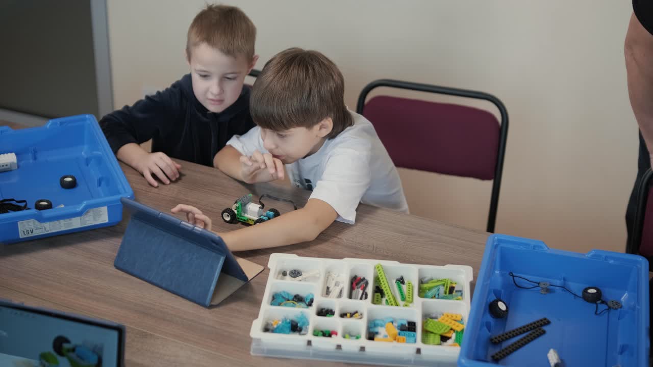 los niños se centraron atentamente en el ensamblaje de piezas de un kit de robótica, con una tableta que muestra instrucciones, promoviendo el aprendizaje y la creatividad del tallo