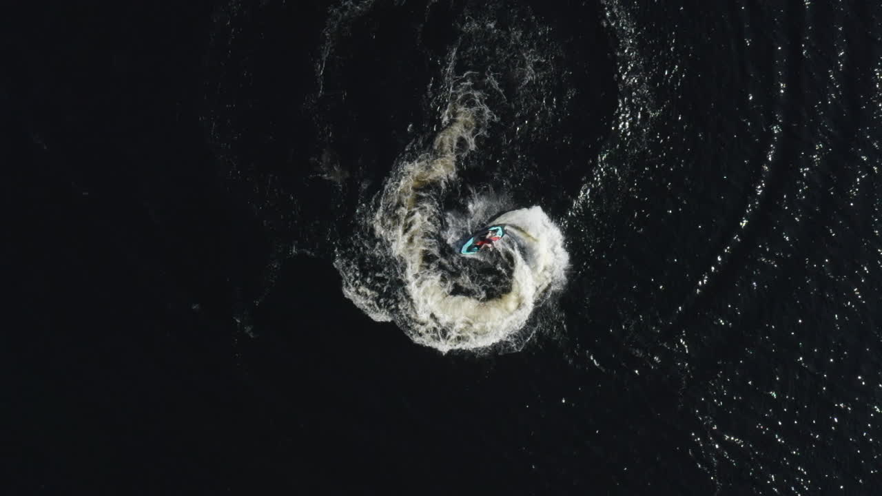 Aerial top down view of a fast water scooter jet ski going around in circles and making beautiful white foamy waves in Sweden
