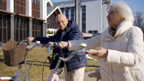 Side-view-of-a-senior-couple-holding-bikes-while-walking-and-talking-in-the-park-on-a-winter-day