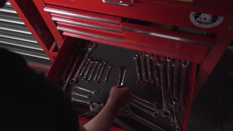 male opening a giant red tool cabinet a grabbing a screwdriver and wrench