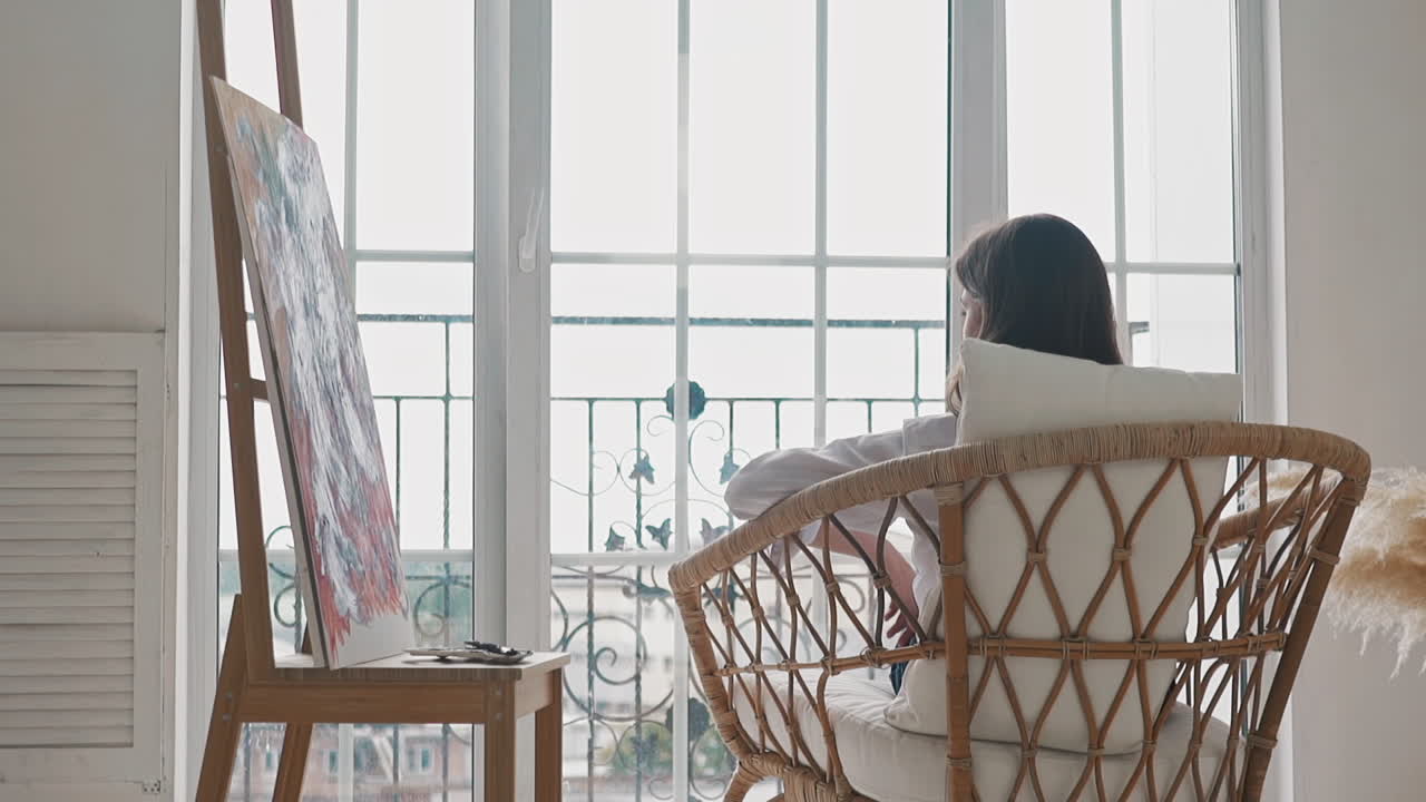 예술가 여성은 작업 후 스튜디오에서 의자에 앉아 휴식을 취합니다.