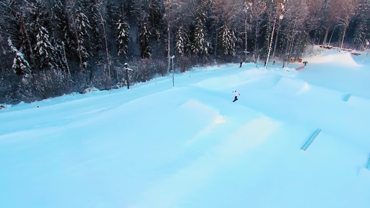 Veduta aerea laterale di uno snowboarder che salta da una pista in uno snowpark di sera.