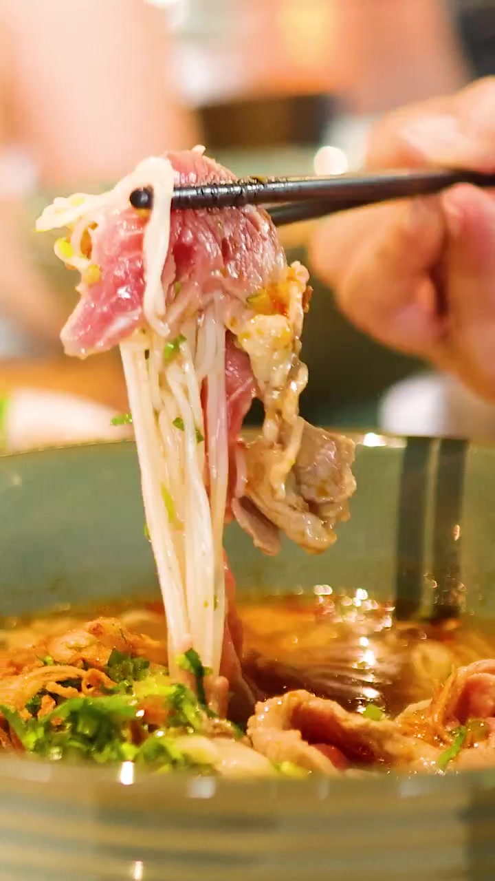 Cận cảnh đũa gắp sợi phở từ tô phở Việt Nam bốc khói, làm nổi bật các nguyên liệu tươi ngon và màu sắc rực rỡ.