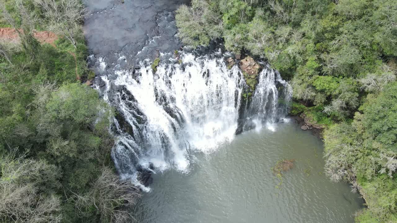 Aerial view of a stunning waterfall surrounded by green forest. Water falls with power, creating mist, peace, and a deep sense of natural beauty and freshness
