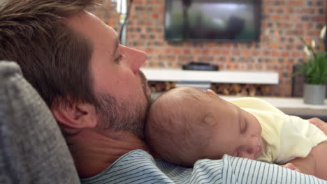 Padre-Sentado-En-El-Sofá-Sosteniendo-A-Su-Hijo-Bebé-Dormido