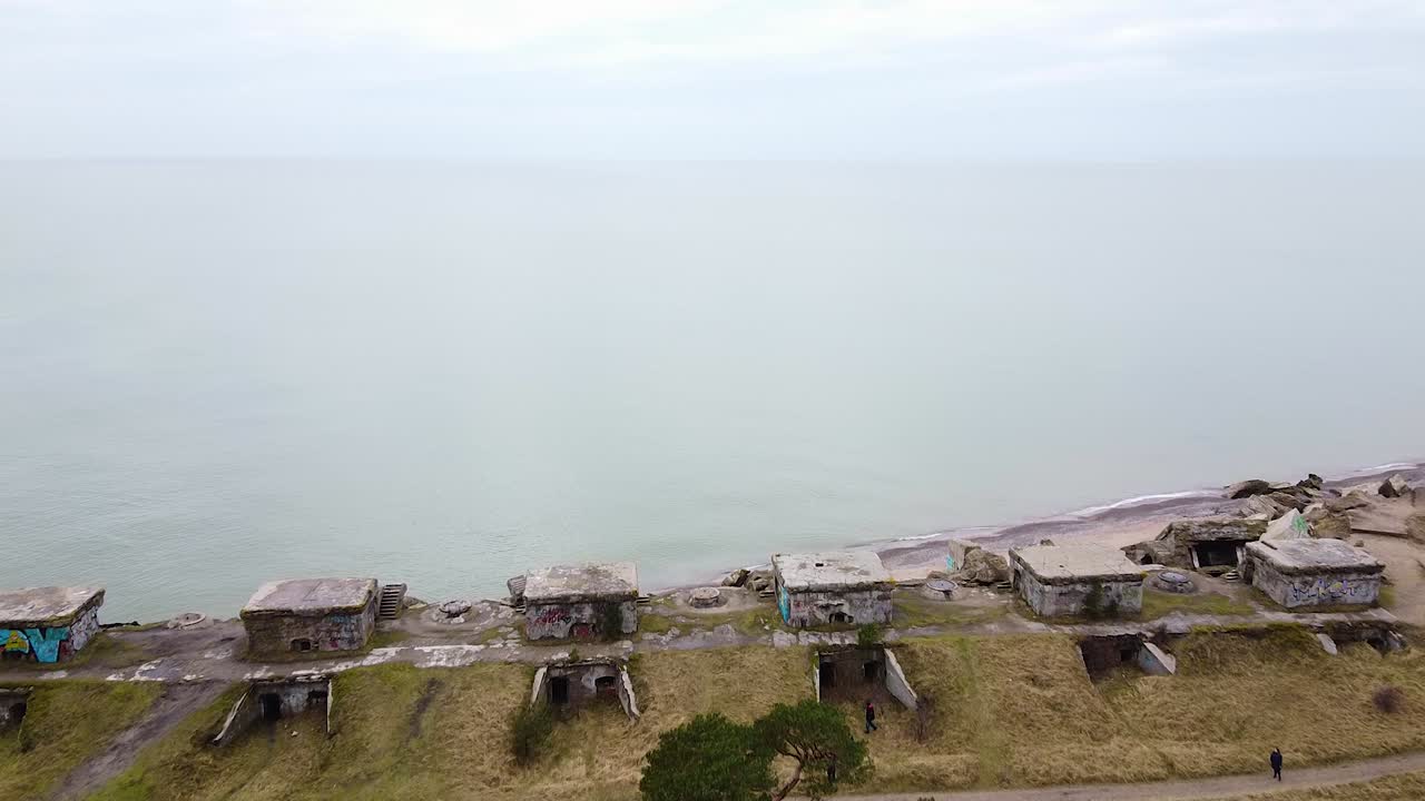 Aerial view of abandoned seaside fortification building at Karosta Northern Forts on the beach of Baltic sea in Liepaja in overcast spring day, pine wood, revealing drone shot moving forward