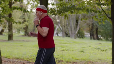 male senior person running along the road in park. mature runner man training, listening music