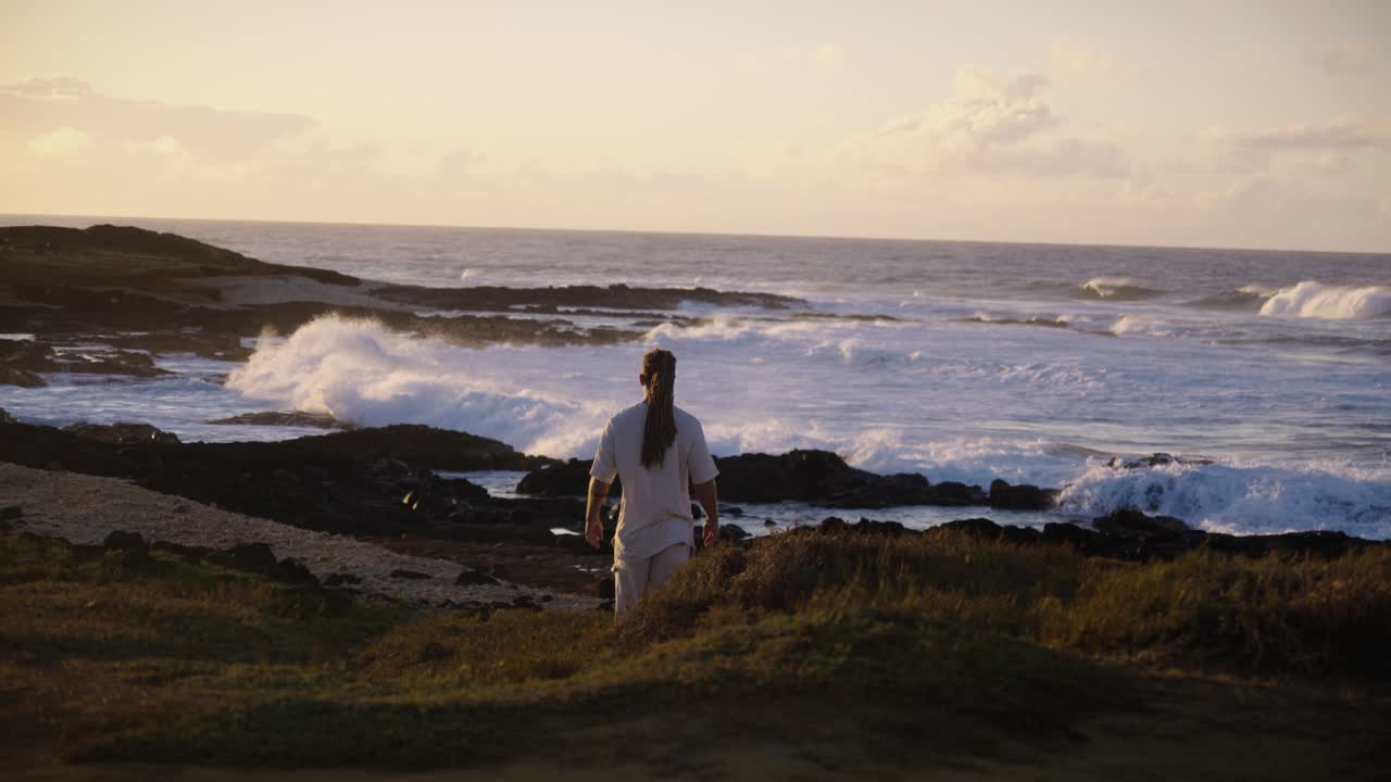 A contemplative man gazes out over the ocean as waves roll toward the rocky coast, bathed in soft golden light, symbolizing peace, reflection, and a deep connection with nature