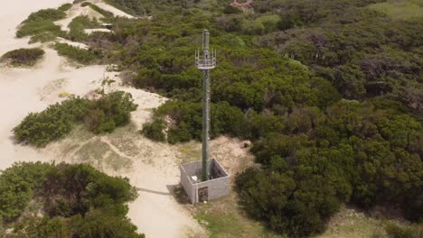 Luftbahnaufnahme-Des-Fernmeldeturms-Am-Sandstrand-Und-Grüne-Buschdünen-An-Sonnigen-Tagen---Mar-De-Las-Pampas,-Argentinien