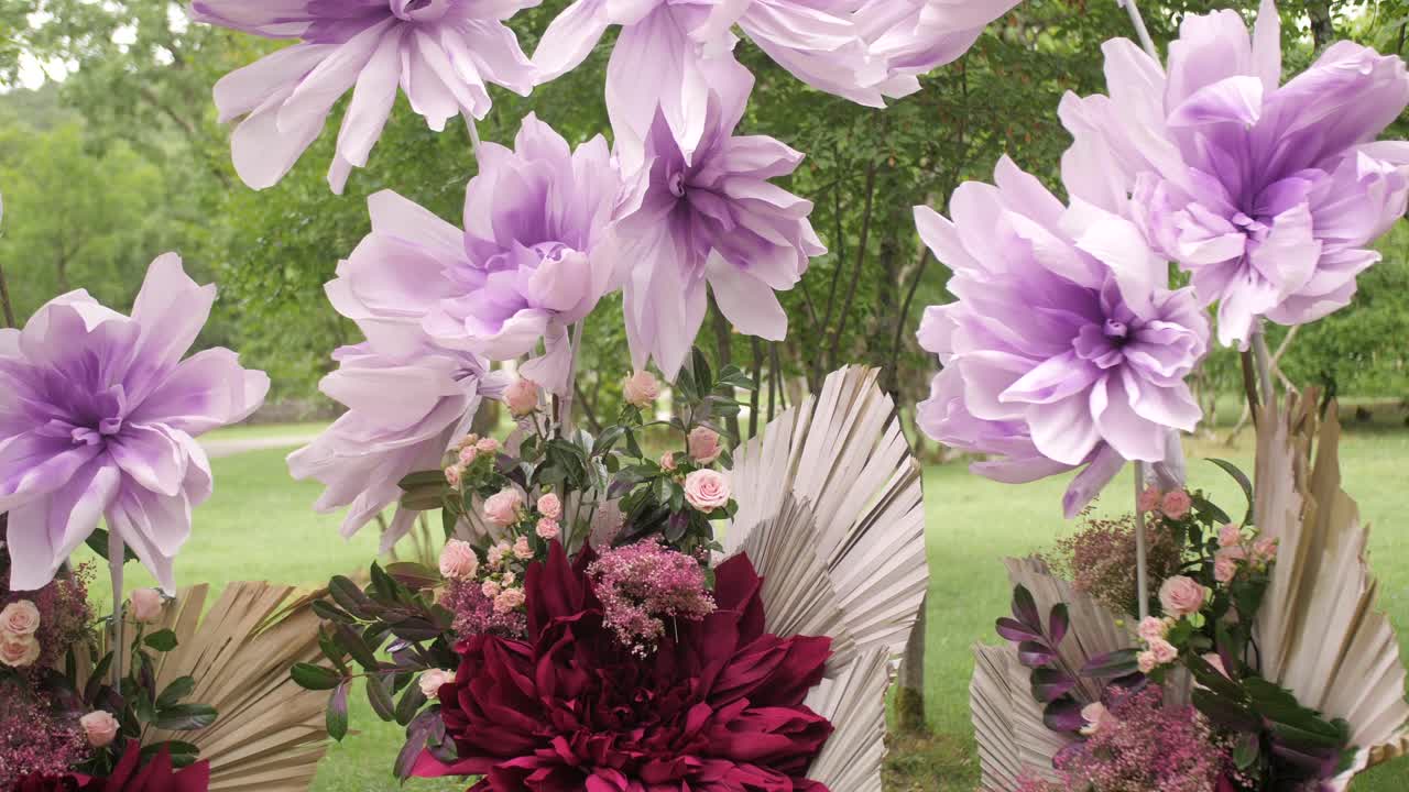 Tilt shot of wedding arch with giant lilac crepe flowers and real roses in bloom, forest setting