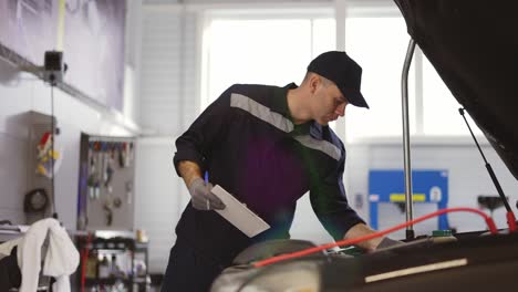 Mechanic-in-a-auto-repair-shot-checking-engine-making-notes-to-his-tablet,-close-up