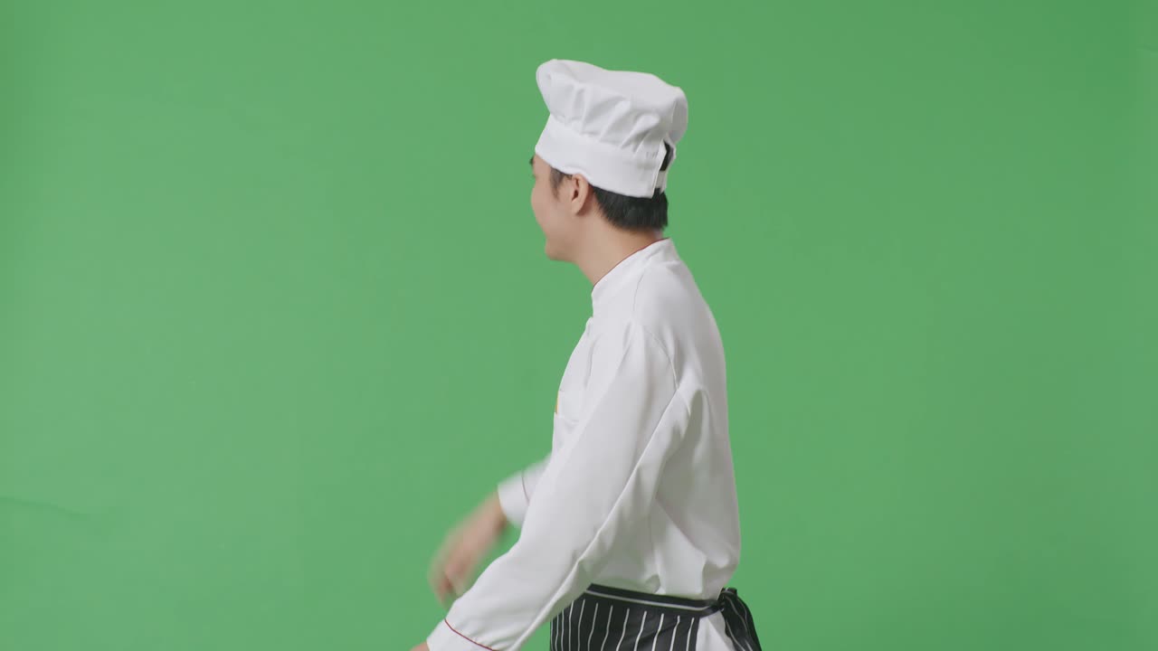 Vista laterale di uno chef asiatico che cammina e saluta con la mano in uno studio con sfondo a schermo verde