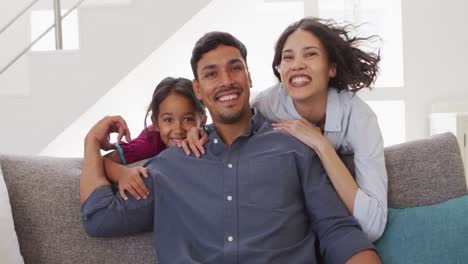 Retrato-De-Padres-Hispanos-Felices-Y-Su-Hija-Abrazándose-En-La-Sala-De-Estar