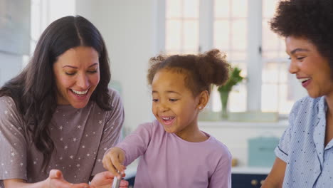 Familie-Mit-Zwei-Müttern-Im-Schlafanzug,-Die-Zu-Hause-Mit-Ihrer-Tochter-Morgenpfannkuchen-In-Der-Küche-Backen