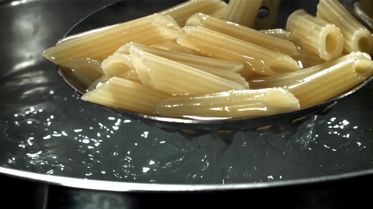 Primo piano di penne che bollono e vengono scolate da una pentola.