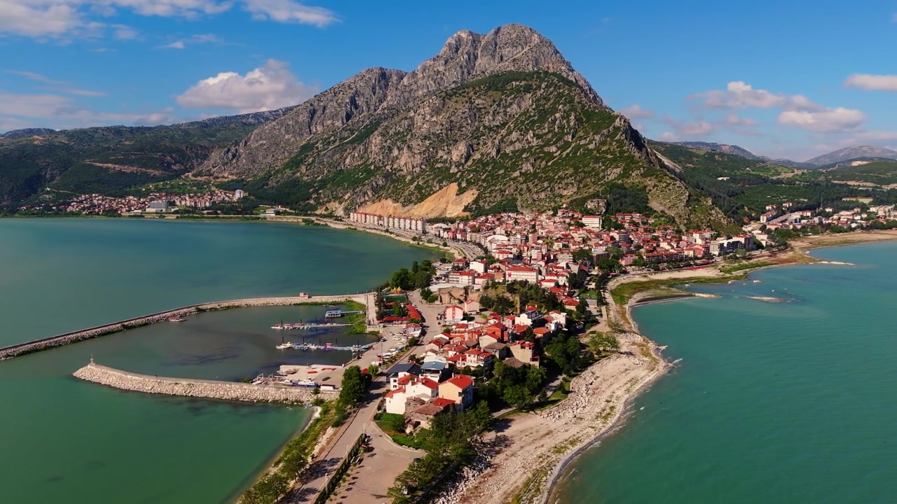 Yüksek açılı drone çekimiyle, arka planda yüksek dağ zirveleri olan yerleşimli Eğirdir Gölü yarımadası. Türkiye'de manzaralı kıyı yerleşimi ve göl kenarı köy manzarası.