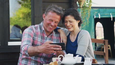 mature couple in garden center cafe taking selfie on mobile phone