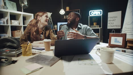 Joyful-afro-man-and-woman-laughing-in-front-of-laptop-screen-at-workplace.