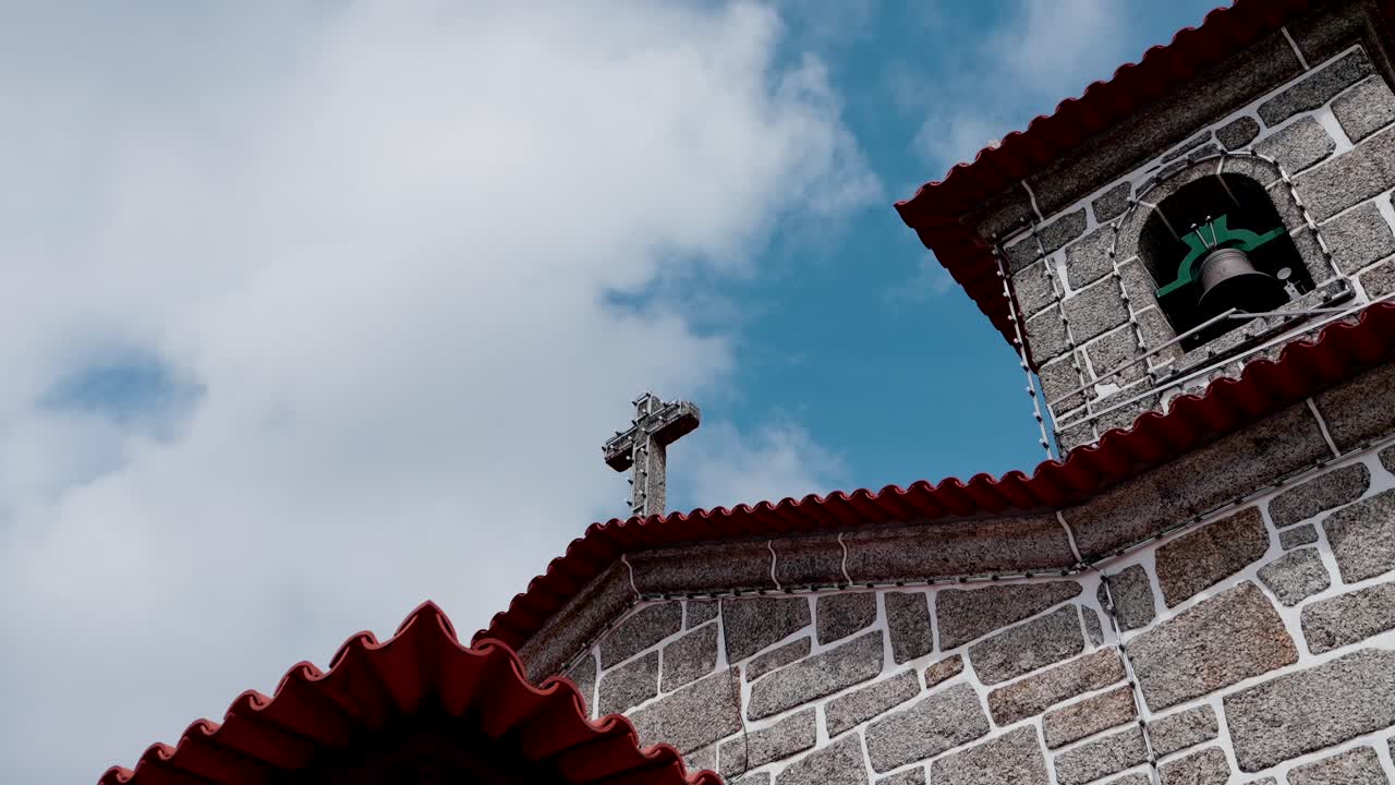 close view of church bell and stone cross with vibrant roof tiles and clouds