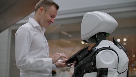 el hombre en el centro comercial se comunica con un asesor robot. tienda moderna y vendedor robot. robot ayuda a un hombre en el centro comercial.