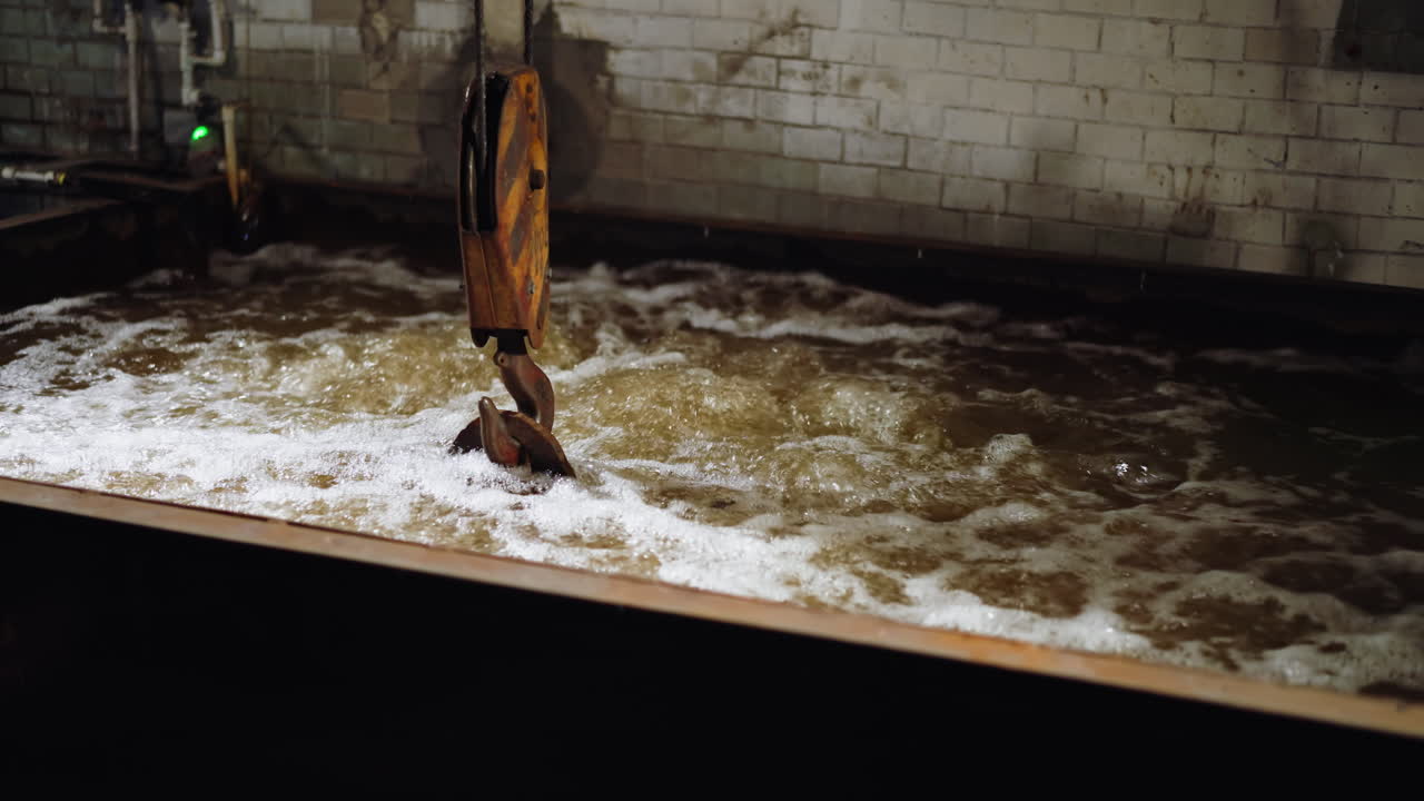 Crane hook stirs turbulent frothy water in a quench tank at a steel manufacturing foundry
