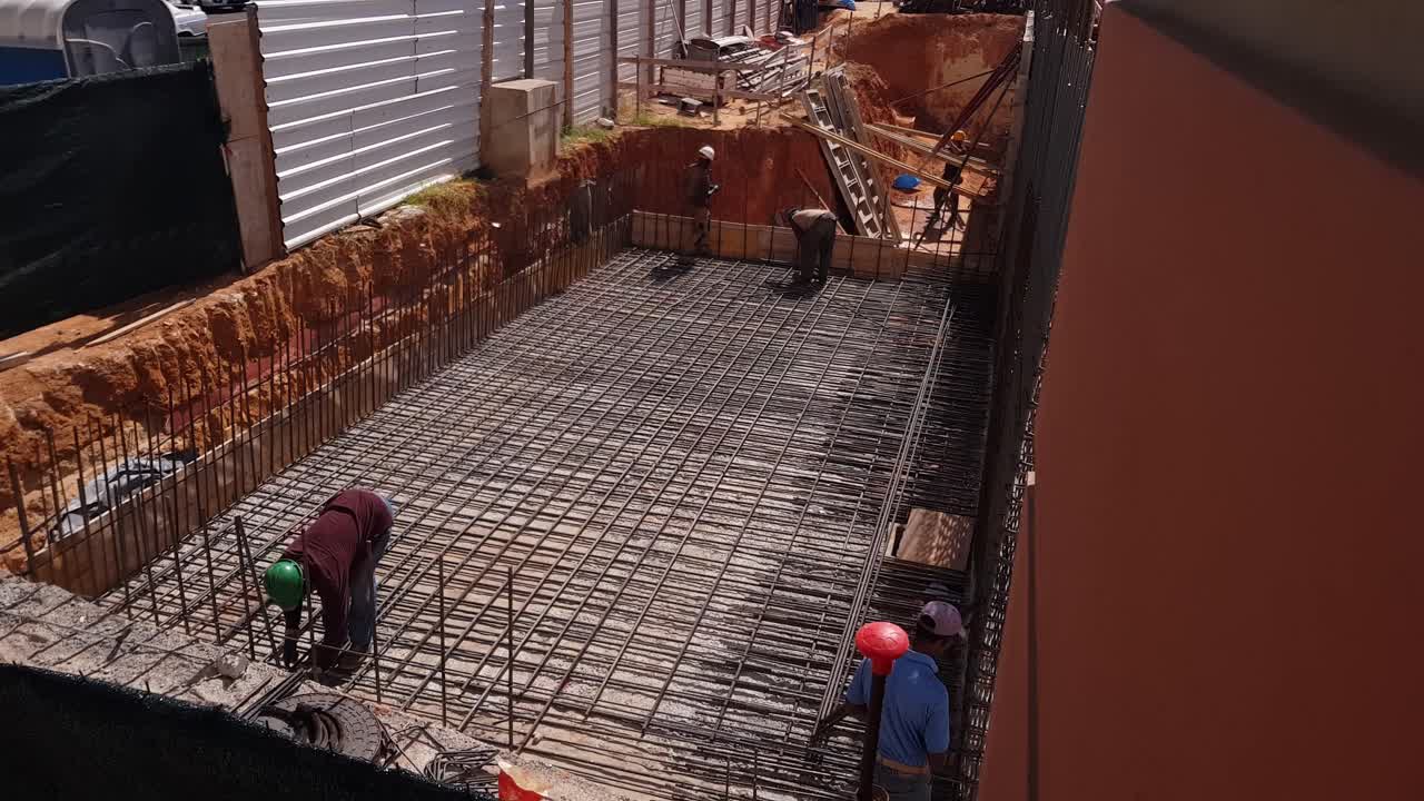 Group of construction workers working on a construction site, attaching reinforcing steel bars on top of the concrete for added support