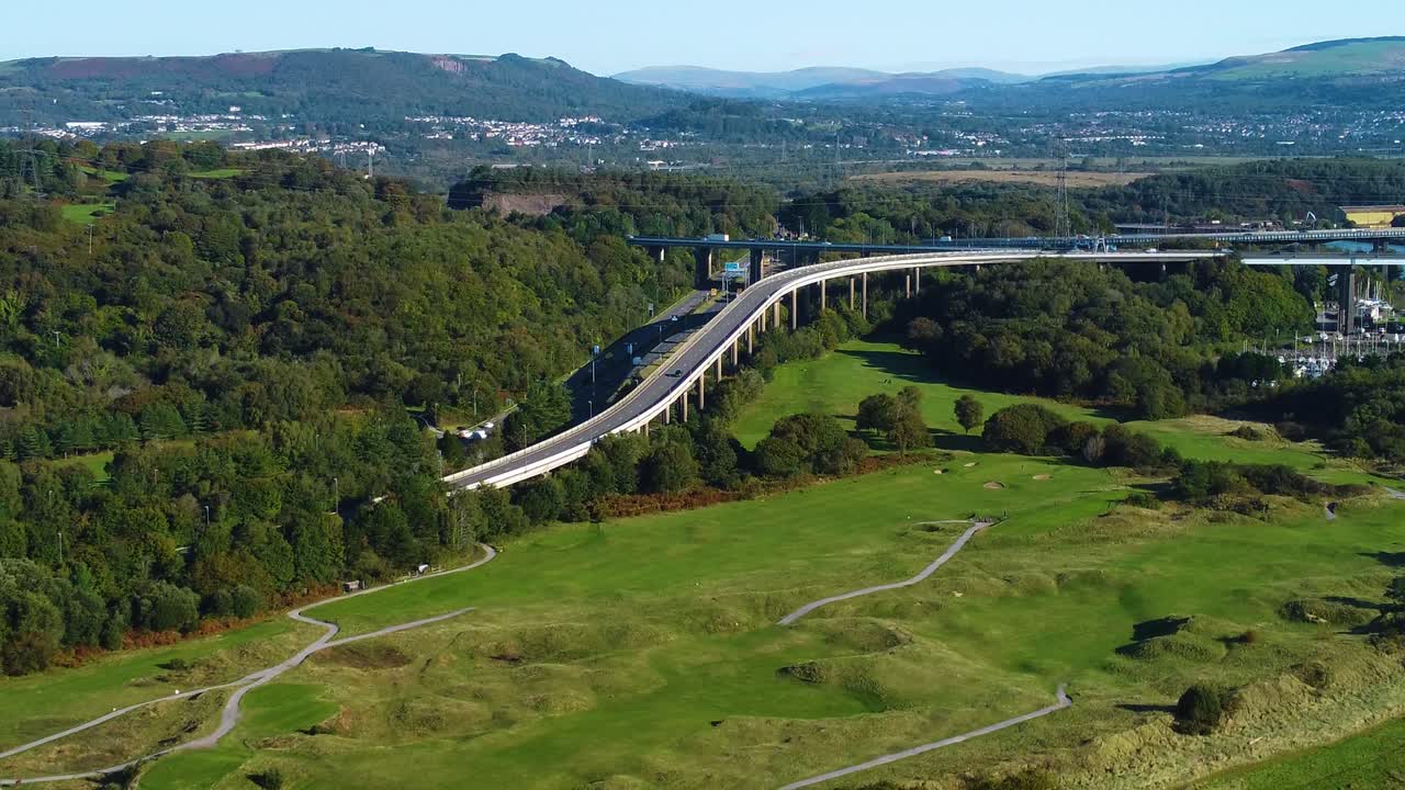 Retreating Aerial Over M4 Motorway Junction 42 Leading to Fabian Way in Swansea with Dense Forest and Mountains in Background with Golf Course Below
