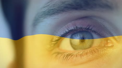 animation of flag of ukraine waving over open eye of caucasisan woman