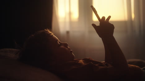 child using smartphone in bed at sunrise or sunset
