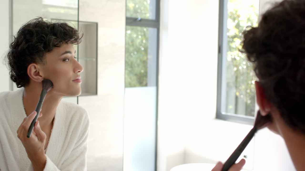 Applying makeup, non binary person using brush while looking in bathroom mirror