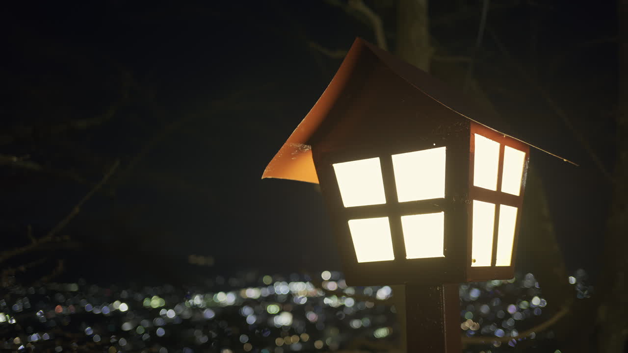 A beautifully crafted outdoor lantern shines brightly against the night sky of Fujikawaguchiko, highlighting a sprawling city below. Chureito Pagoda park