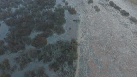 vista aérea de aguas altas, inundación del río durbe, agua marrón y fangosa, campos agrícolas bajo el agua, día de invierno nublado con nieve ligera, disparo de drone de ojo de pájaro avanzando