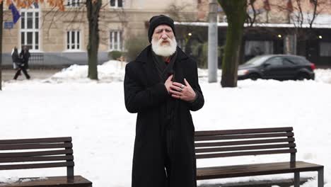 An elderly man standing outside has chest pains or a heart attack. Stroke in winter. Healthcare concept.
