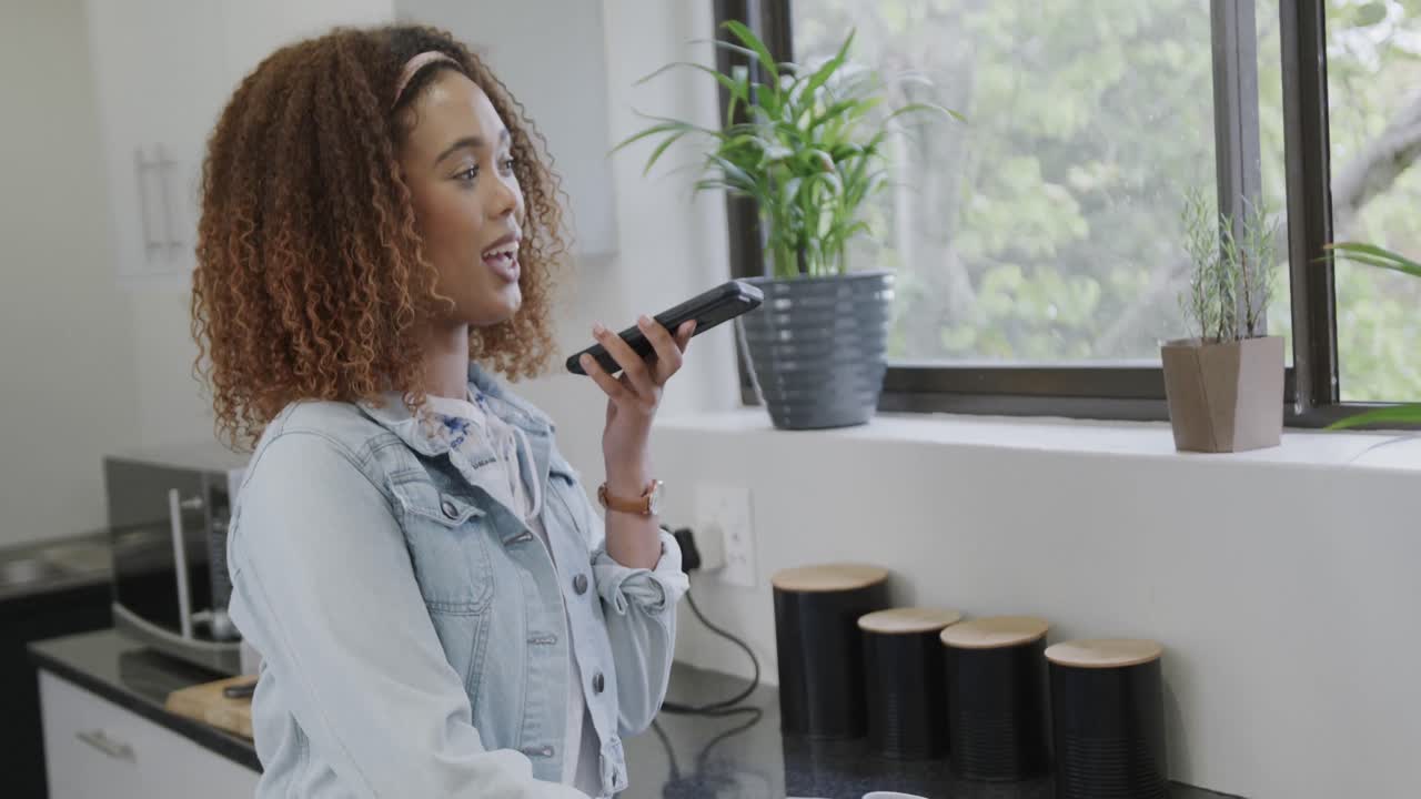 Happy biracial woman talking on smartphone in kitchen, slow motion