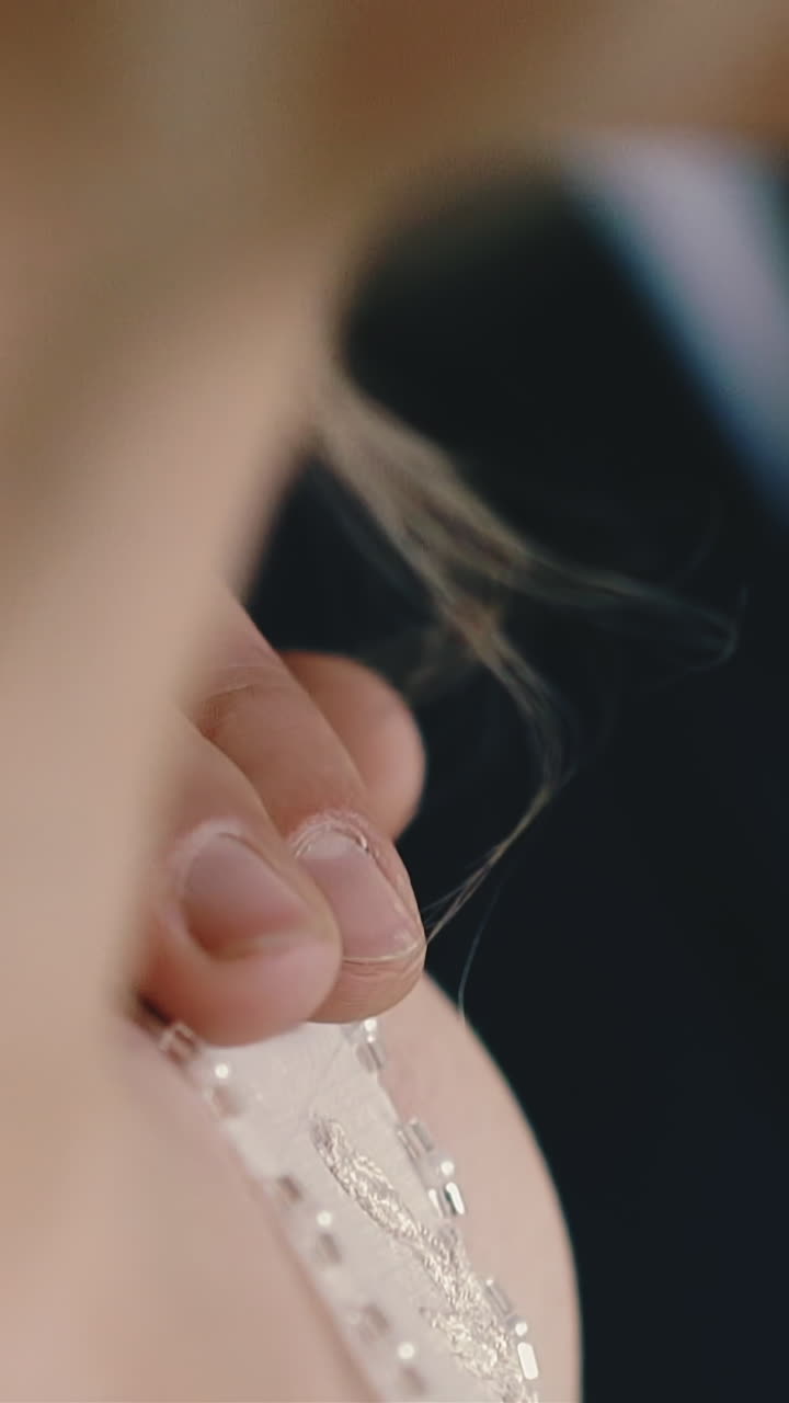 CU shot, slow motion: young man in dark suit puts hand on shoulder of bride wearing wonderful wedding dress in light room extreme close view