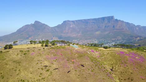 Antena-Drone-Sobre-Parapente-Y-Parapentes-Con-Table-Montaña-Cape-Town-South-Africa-En-Segundo-Plano.