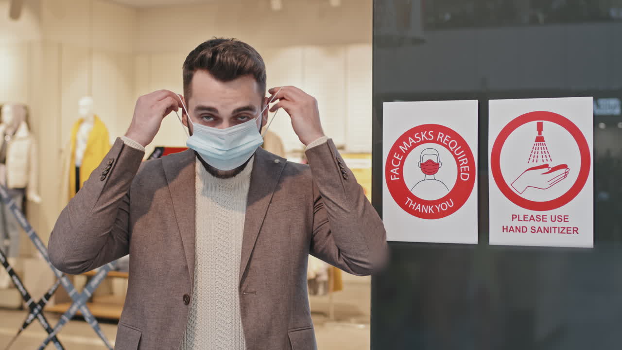 Portrait Of Man Putting On Face Mask At Shopping Centre