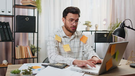 indian businessman work on laptop sticky notes with many tasks inscription overworked at office