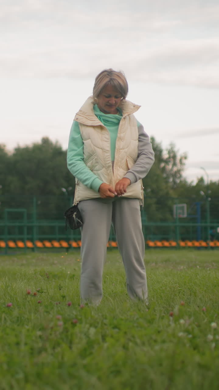 Woman prepares outdoors, Woman adjusting clothing in park, Woman adjusting her outfit before stroll in overcast park, Lady securing her accessories and adjusting apparel during calm park evening