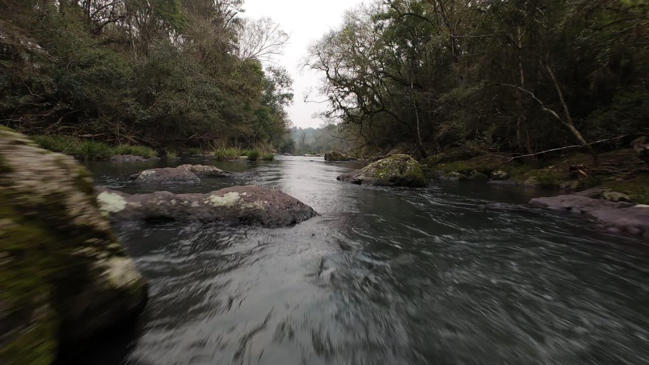 River flowing through a rocky landscape in Misiones, Argentina, showcasing the natural beauty of Gruta India with lush vegetation and dynamic water movement, FPV drone footage